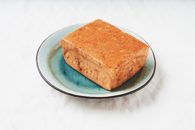Kostka organicznego sera somoked tofu podawana na niebieskim talerzu na bambusowej macie. Koncepcja wegańskiej przekąski