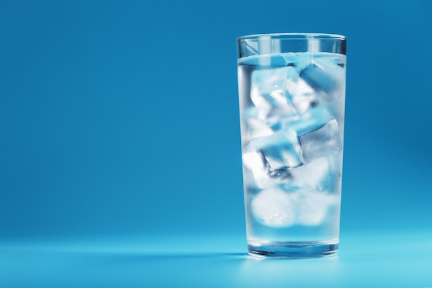 Kostki lodu w szklance z krystalicznie czystą wodą na niebieskim tle. Orzeźwiająca i zdrowa woda w upalne dni