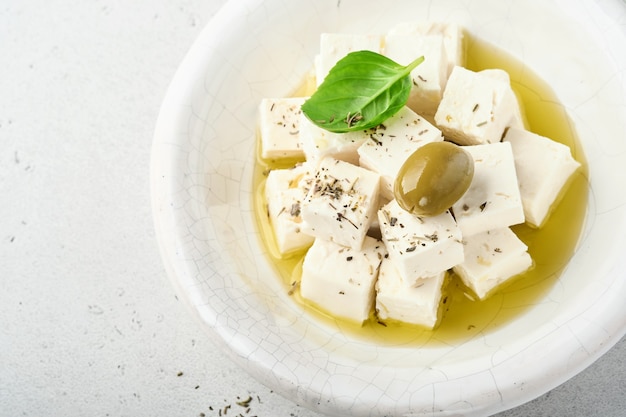 Kostki sera feta z rozmarynem, oliwkami i oliwą na jasnoszarej powierzchni.