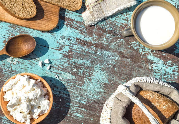 Kosz, szklanka mleka, twarożek i chleb na stole z jasnoniebieskich desek. Widok z góry