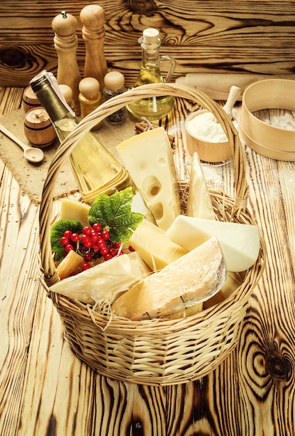 Kosz z różnymi rodzajami sera i wina na drewnianym tle