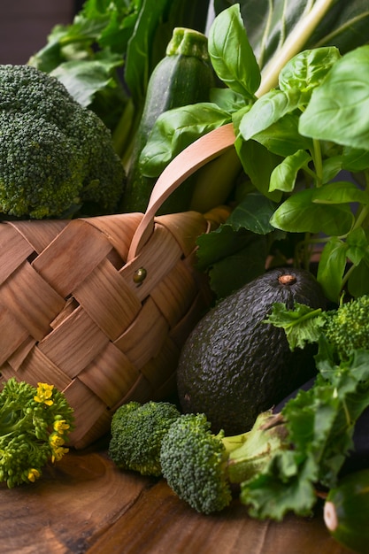 Zdjęcie kosz ze świeżych zielonych warzyw na drewnianym tle. awokado, brokuły, cime di rapa inne warzywa. wolne miejsce na tekst. skopiuj miejsce