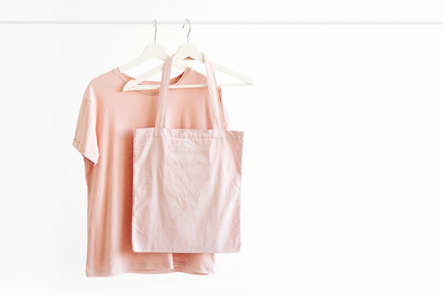 Koszulka w pastelowym różowym kolorze na wieszaku z eko torbą na białym tle.