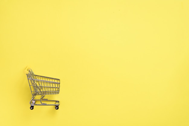 Koszyk na żółtym tle. Styl minimalizmu. Wózek sklepowy w supermarkecie. Sprzedaż, rabat, koncepcja shopaholism. Trend społeczeństwa konsumpcyjnego