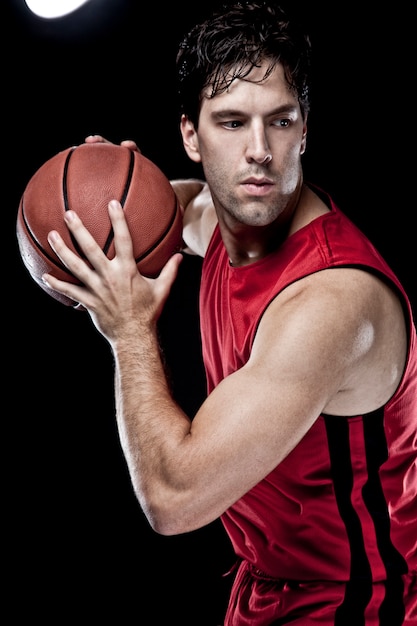 Koszykarz z piłką w dłoniach i czerwonym mundurze. studio fotograficzne.