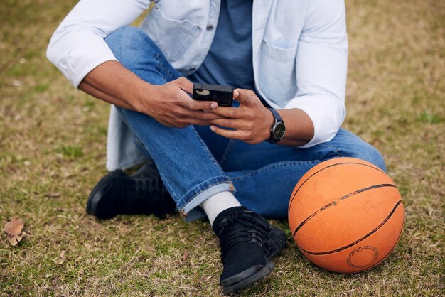 Koszykówka i bity to wszystko, czego naprawdę potrzebujesz. Ujęcie nierozpoznawalnego mężczyzny korzystającego ze smartfona na zewnątrz uczelni.