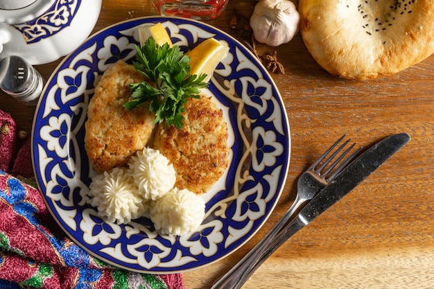 Kotlety rybne z puree ziemniaczanym, cytryną i natką pietruszki na talerzu z tradycyjnym uzbeckim wzorem.