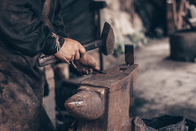 Kowal przetwarza metal młotkiem na kowadle w kuźni Kowal w brudnych ubraniach uderza w żelazo w warsztacie Obróbka metali