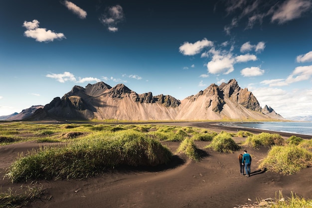 Krajobraz góry Vestrahorn i kopiec trawy na czarnej, piaszczystej plaży w słoneczny dzień na półwyspie Stokksnes Islandia