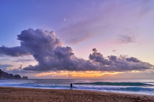Krajobraz malowniczego idyllicznego spokojnego spokojnego nieba tapety z puszystymi chmurami i sylwetką osoby stojącej samotnie na wybrzeżu morza i piaszczystej plaży