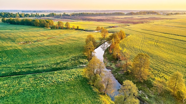 Zdjęcie krajobraz wiosennego poranka spokojna rzeka na kwitnących łąkach widok z lotu ptaka na tereny wiejskie z góry rolnicze żółtozielone pola rzepaku scena z kwiatami rzepaku i mniszka lekarskiego