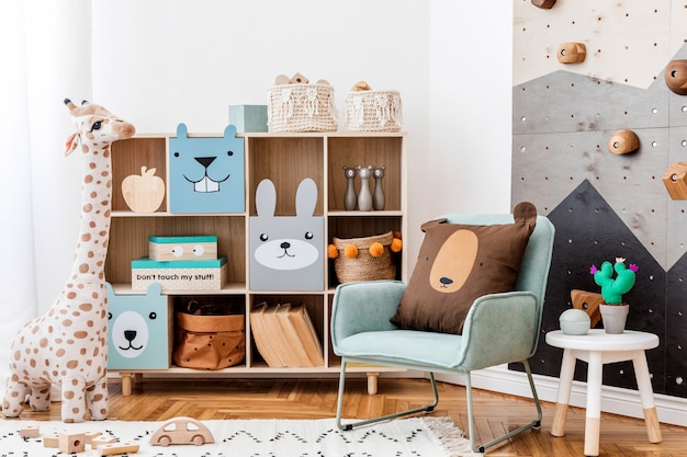 Kreatywna kompozycja stylowego i przytulnego wystroju wnętrza pokoju dziecięcego scandi z grafiką na ścianie zabawki i zabawki pluszowe sofa komoda fotel dywan i akcesoria biała ściana i parkiet
