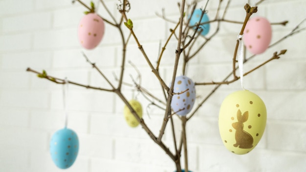 Kreatywna kompozycja z jajkami wielkanocnymi wiszącymi na gałęziach drzew w pobliżu białej ceglanej ściany