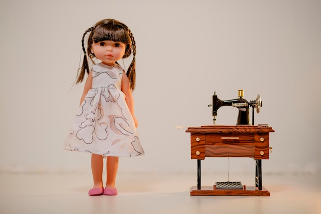 Kreatywna sesja zdjęciowa z uroczą lalką stojącą obok zabawkowej maszyny do szycia Urocza sesja zdjęciowa lalek
