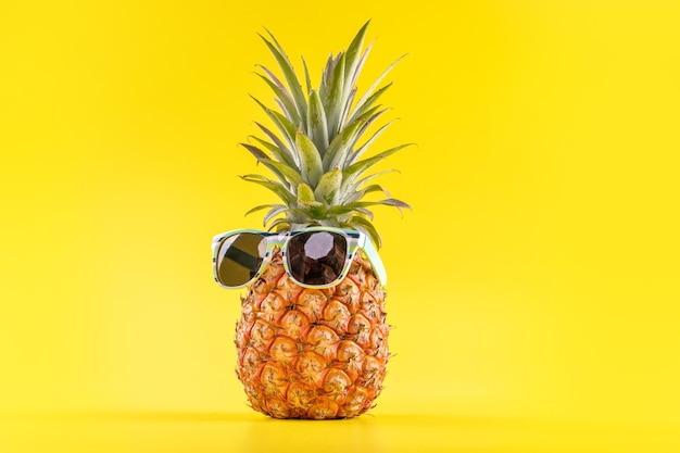 Kreatywne ananasy z okularami przeciwsłonecznymi na białym tle na żółtym tle, wzór projektu letnich wakacji na plaży, miejsce na kopię, z bliska, puste dla tekstu