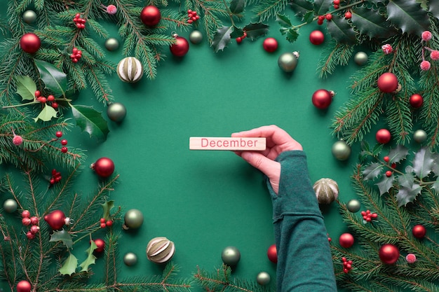 Kreatywne świąteczne mieszkanie leżało na zielonym papierze. Żeńska ręka trzyma drewnianego słowo.