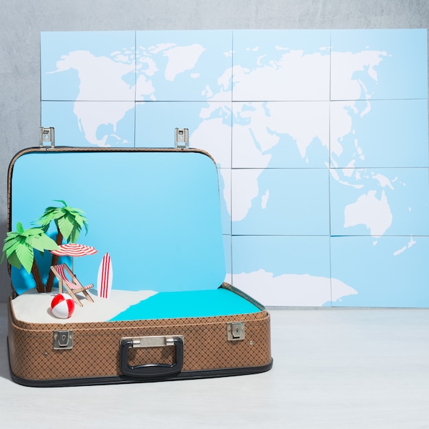 Kreatywne ułożenie zabawkowego układu plaży wewnątrz walizki na tle mapy świata