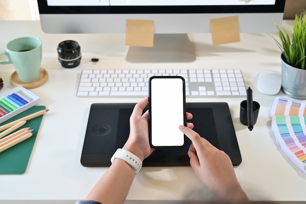 Kreatywnie projektant trzyma mobilnego mądrze telefon w pracownianym miejscu pracy i używa