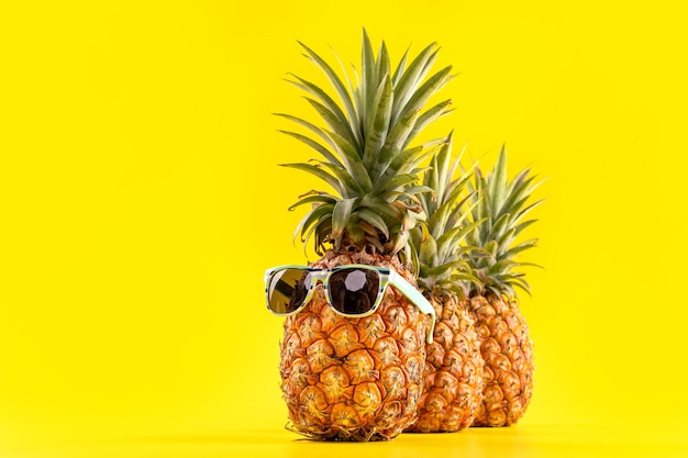 Kreatywny ananas patrząc w górę z okularami przeciwsłonecznymi i muszlą na białym tle na żółtym tle, kopia przestrzeń z bliska