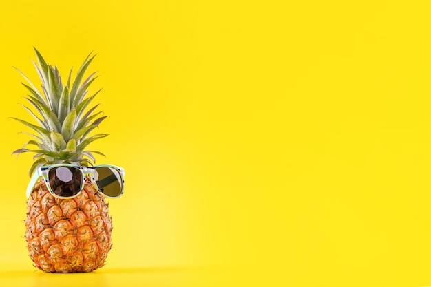 Kreatywny ananas patrząc z okularami przeciwsłonecznymi i powłoką na białym tle na żółtym tle letnie wakacje plaża pomysł projekt wzór kopia przestrzeń z bliska