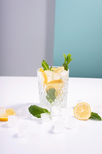 Kreatywny letni koktajl z lodem w szklanej szklance z miętą cytrynową i kostkami lodu na białoniebieskim tle