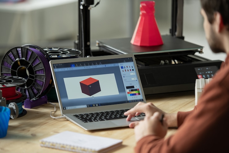 Zdjęcie kreatywny projektant pracuje nad nowym modelem 3d na ekranie laptopa przed wydrukowaniem go na specjalnym sprzęcie w biurze