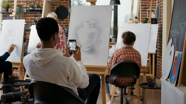 Kreatywny student biorąc obraz szkic wazon na smartfonie w klasie sztuki. Młody człowiek za pomocą telefonu komórkowego, aby zrobić zdjęcie i zapamiętać technikę umiejętności rysowania na lekcji edukacyjnej.