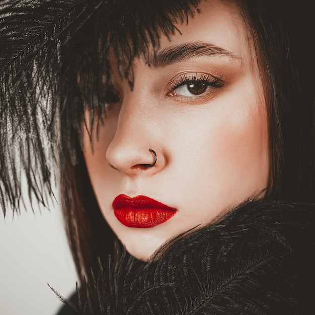 Kreatywny stylowy portret dziewczyny kaukaski model z czerwonymi ustami i czarnymi piórami wokół głowy, widok z boku. Pojęcie piękna.