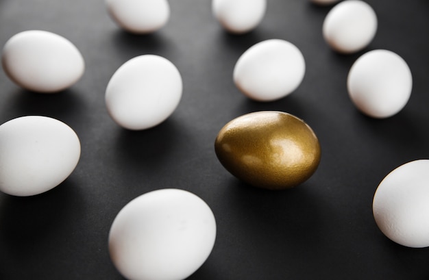 Zdjęcie kreatywny wzór wykonany z naturalnych białych jaj kurzych i jednego złotego malowanego jajka na czarnym tle