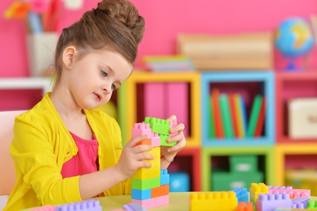 Kręcona dziewczynka bawi się kolorowymi plastikowymi klockami