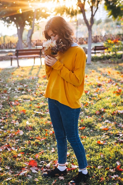 Kręcona młoda dziewczyna w żółtym swetrze na trawie z jesiennym bukietem suchych liści i kwiatów