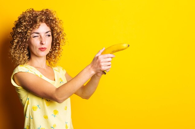 Kręcona Młoda Kobieta Trzymająca Banana Z Pistoletem Na żółtym Tle