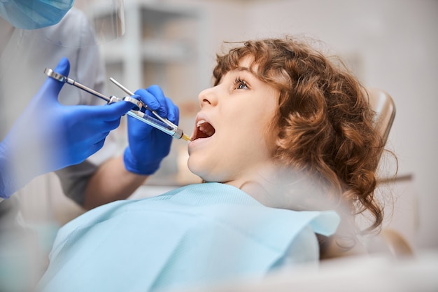 Kręcone Dziecko Siedzi Na Fotelu Dentystycznym Z Otwartymi Ustami I Dostaje Zastrzyk Ze Znieczuleniem Od Dentysty