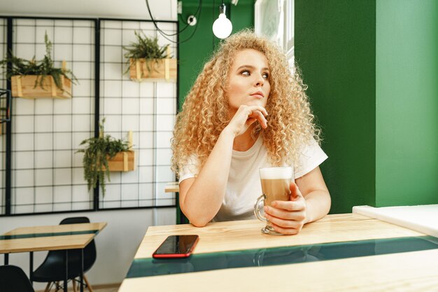 Kręcone młoda kobieta siedzi przy stole w kawiarni i relaks przy filiżance kawy