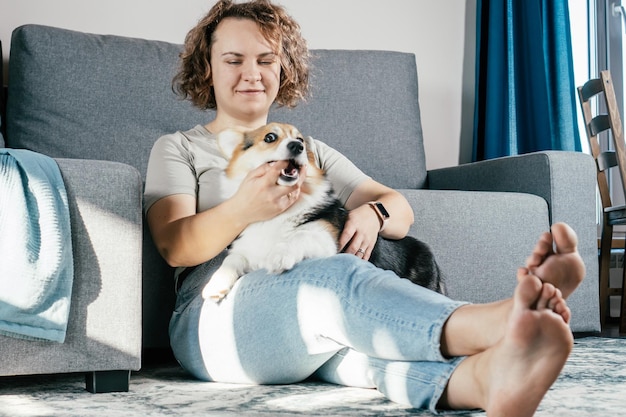 Kręcone włosy zadowolona wesoła boso kobieta z psem corgi Trening posłuszeństwa karmienie zwierząt siedzących i bawiących się