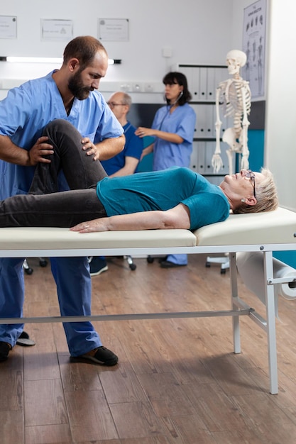 Kręgarz próbujący zmniejszyć nacisk na kolano pacjenta z zapaleniem stawów i bólem. Asystent medyczny łamiący kości nóg dla ulgi i fizycznego powrotu do zdrowia emerytowanej kobiety z bólem.