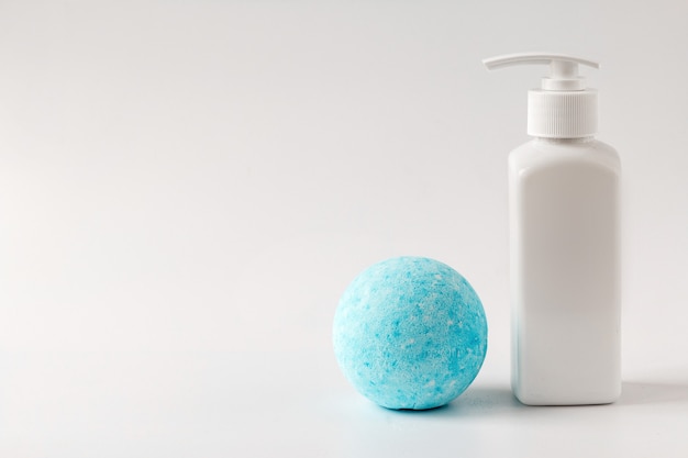 Kremy kosmetyczne w białej plastikowej butelce i niebieska bomba do kąpieli na białym stole