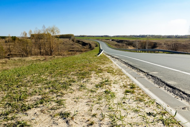 Kręta autostrada ciągnąca się w oddali na tle pięknego wiosennego krajobrazu, pól, łąk, lasów i wzgórz. Pasy drogowe na asfalcie. Perspektywa wyjazdu w podróż.