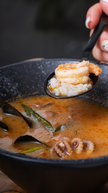 Zdjęcie krewetki i ryż na łyżce w kobiecej ręce na tle zupy tom yum