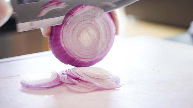 Krojenie fioletowej cebuli na białą deskę do krojenia.