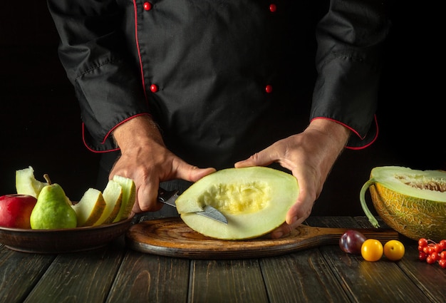 Krojenie melona na stole kuchennym rękami szefa kuchni do menu owocowego w restauracji Koncepcja diety owocowej na ciemnym tle