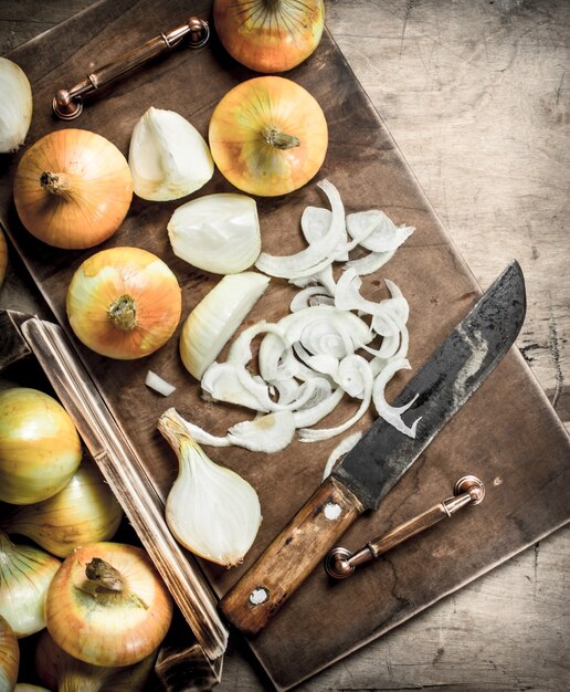 Zdjęcie krojenie świeżej cebuli na deskę do krojenia starym nożem na drewnianym tle