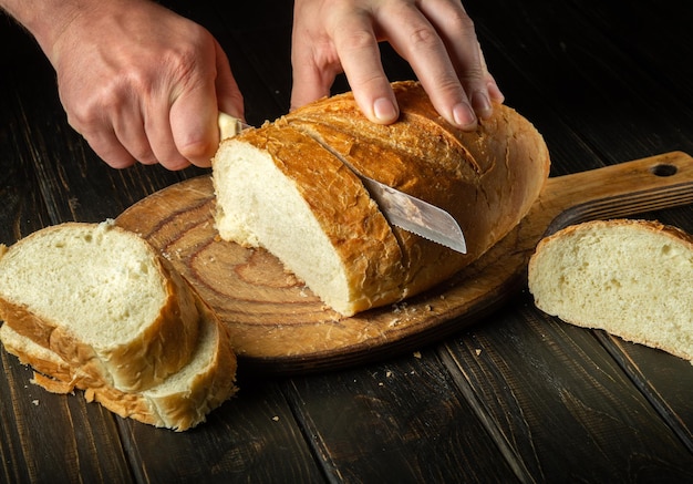 Krojenie świeżo upieczonego chleba pszennego nożem przez ręce kucharza Naczynie narodowe w kuchni