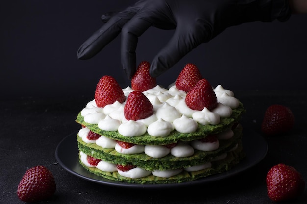 Krok po kroku przygotowanie zielonego ciasta ze szpinaku i truskawek Ostatni krok Ręczna cukierniczka w czarnych rękawiczkach dekorująca ciasto