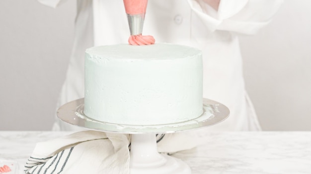 Krok po kroku. Wytłaczane rozetkami buttercream na wierzchu okrągłego trójwarstwowego ciasta waniliowego.