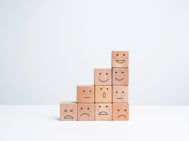 Kroki rozwoju biznesu z radosnymi i smutnymi emocjami na twarzach emotikonów układają się na drewnianych klockach na białym tle, w minimalistycznym stylu. Satysfakcja, ocena, koncepcja badania oceny.