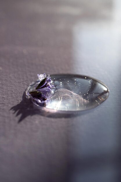 Kropla żelu kosmetycznego z kwiatem lawendy na fioletowym tle