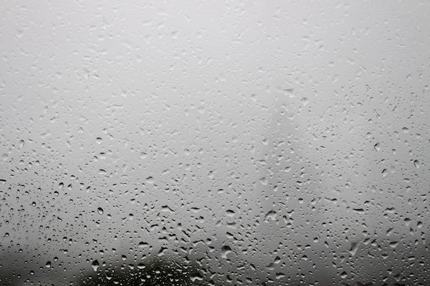 Krople deszczu na szybie okiennej z białą mgłą na tle balkonu