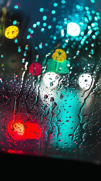 Zdjęcie krople deszczu na szybie samochodu i światłach nocnych.
