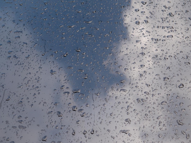 Krople wody na masce metalicznego czarnego samochodu i odbicie chmur i nieba po burzy